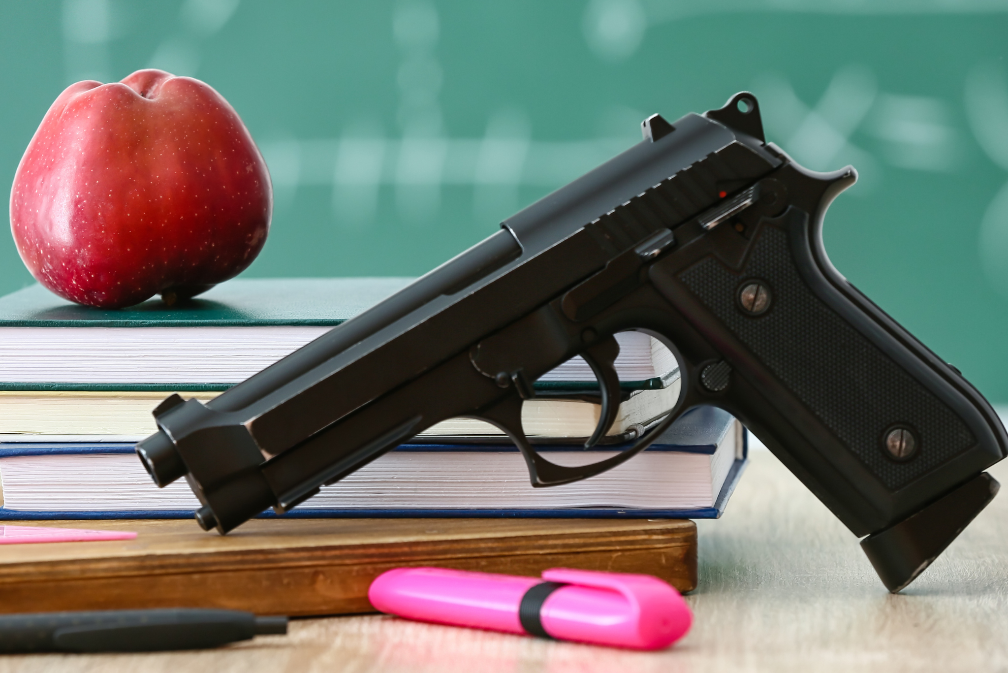 school gun table with an apple, pens, books, and a gun